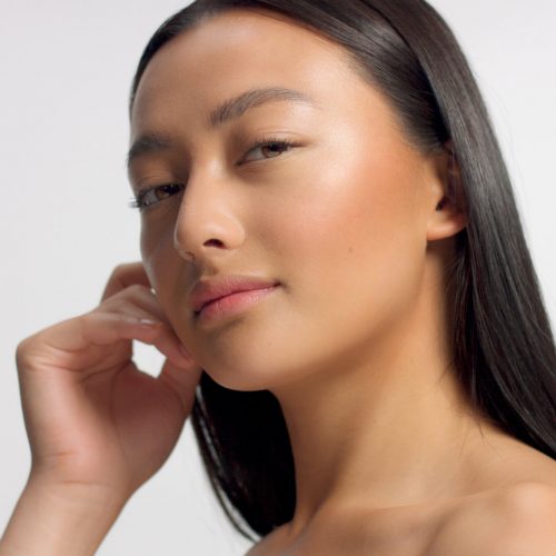 mixed race asian model in studio beauty shoot Model poses to a camera, straight hair Ideal skni and no makeup makeup Head and shoulders crop touches her skin with hand