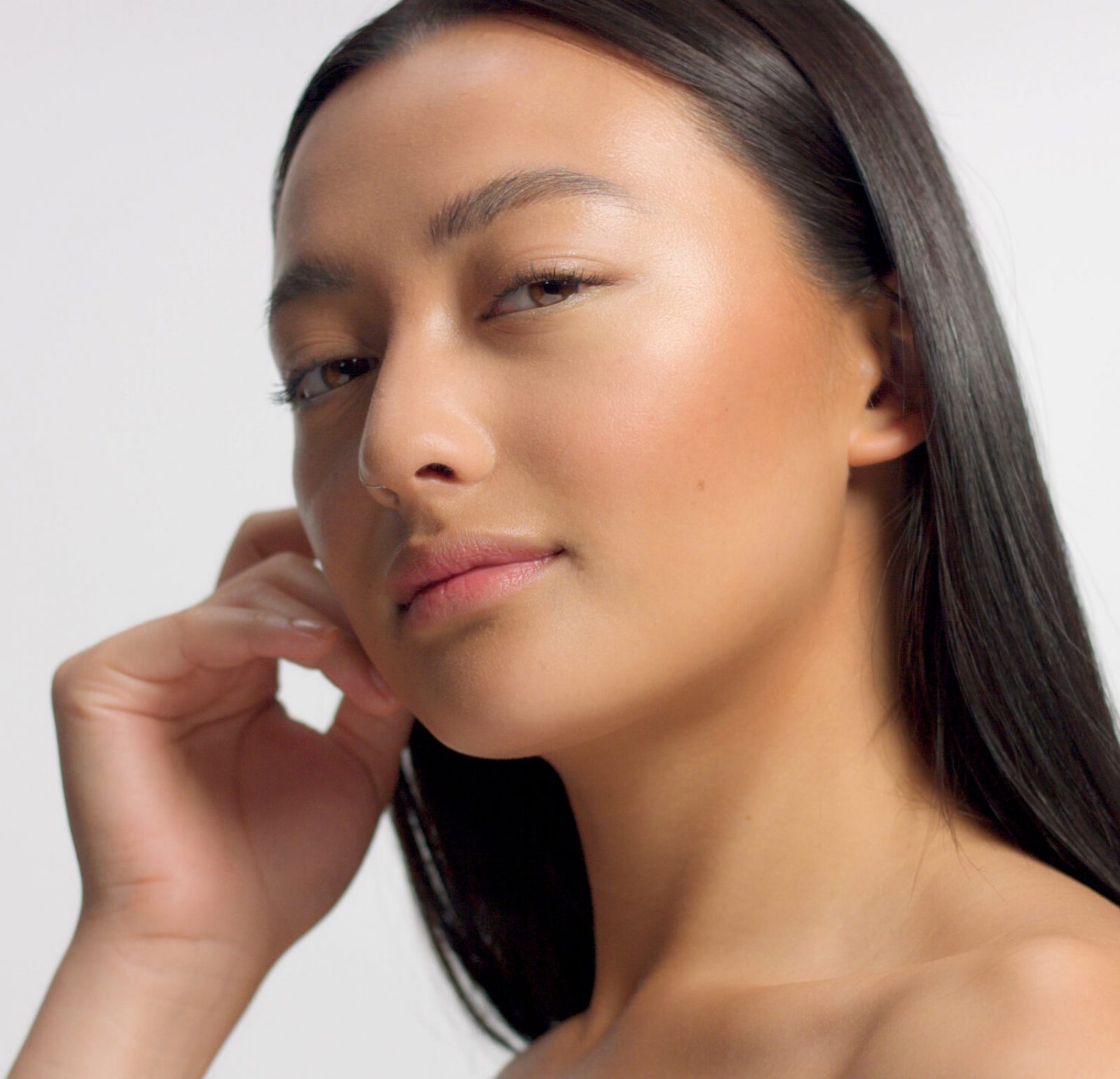 mixed race asian model in studio beauty shoot Model poses to a camera, straight hair Ideal skni and no makeup makeup Head and shoulders crop touches her skin with hand